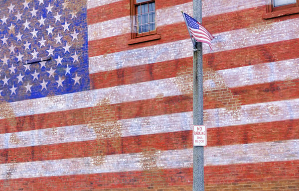 Small-town street scene in Illinois American flag flapping in breeze by huge painted American flag fading from brick wall labor day