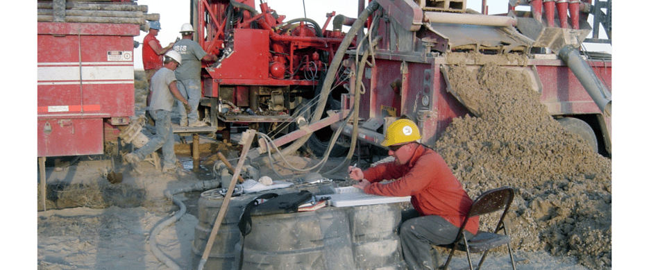 Oil field worker in a yellow hard hat sitting in a chair doing paperwork.