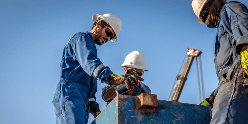 Three oil and gas workers wearing hard hats and safety clothing while working on offshore equpiment.