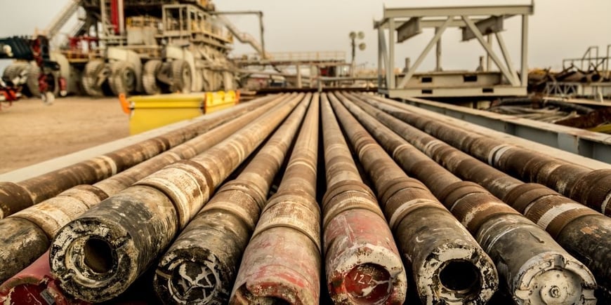 Rows of steel drilling pipes laid out on a pipe rack at an oil and gas drilling rig site, showing the tool joints and pipe body used in rotary drilling operations